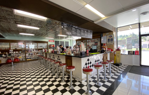 A retro diner interior with a checkered floor, bar stools, and a menu board, featuring staff behind the counter.