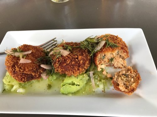Three golden-brown croquettes on a white plate, garnished with herbs and served on a green sauce. One is cut open.