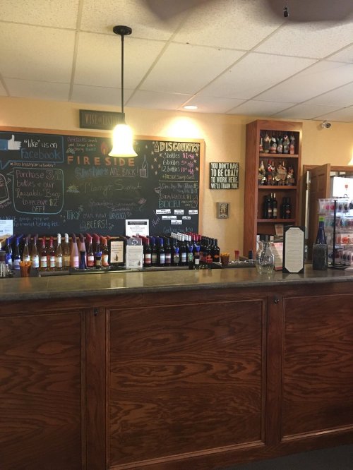 A cozy bar with a wooden counter, chalkboard menu, and shelves of drinks in a warm, inviting atmosphere.