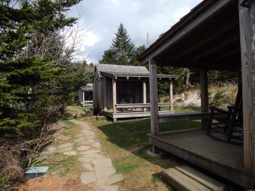 Two rustic wooden cabins surrounded by trees, with a stone path leading through a grassy area.