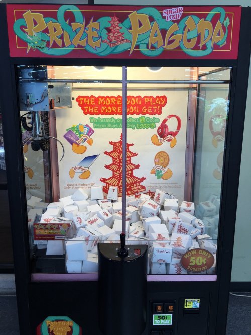 A colorful claw machine filled with white boxes and prizes, labeled "Prize Pagoda." Play for 50 cents.