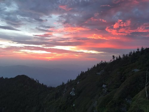 A vibrant sunset paints the sky in shades of pink and orange over a mountainous landscape with trees.