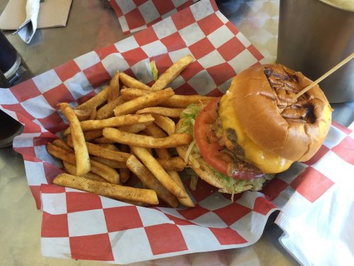 A delicious cheeseburger with lettuce and tomato, served with a side of golden fries on a checkered paper.