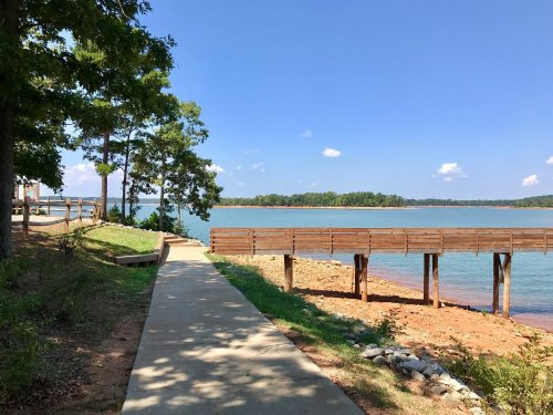 A serene lakeside view with a wooden pier, surrounded by trees and a clear blue sky.