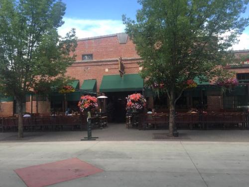 A brick building with green awnings and vibrant flower arrangements, featuring outdoor seating under trees.