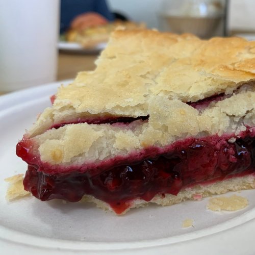A slice of pie with a flaky crust and a vibrant red fruit filling, resting on a paper plate.