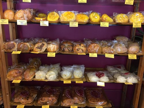 A display of various baked goods in clear packaging on wooden shelves, labeled with yellow tags.