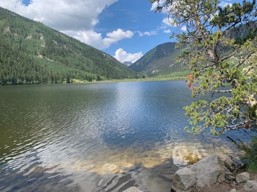 A serene lake surrounded by green mountains and trees under a partly cloudy sky.