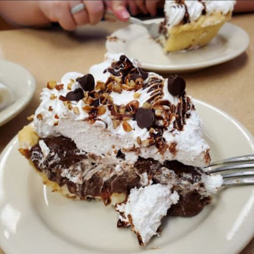 A slice of chocolate cream pie topped with whipped cream, chocolate drizzle, and nuts on a plate.