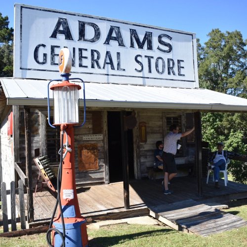 A rustic general store with a sign reading "ADAMS GENERAL STORE," featuring a porch and vintage gas pump.