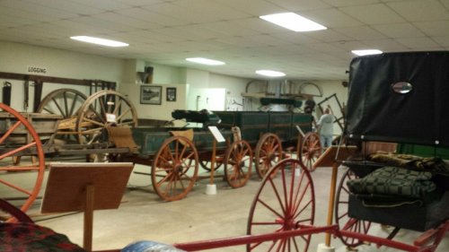 A museum interior featuring vintage wagons and carriages displayed on a concrete floor.