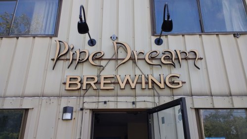 Sign for Pine Dream Brewing on a building exterior, featuring decorative lettering and outdoor lighting.