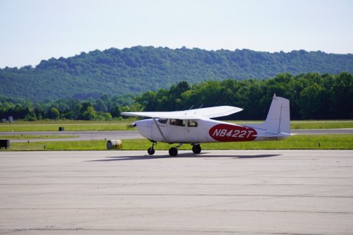 A small airplane with the registration number NB422T parked on a runway, surrounded by green hills and clear skies.