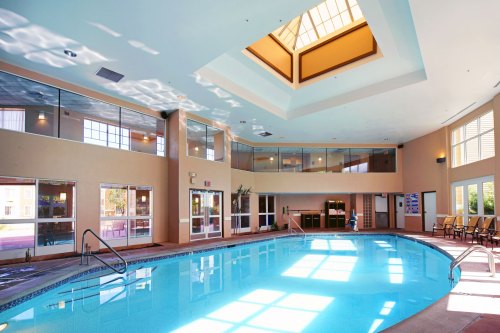 Indoor swimming pool with clear blue water, surrounded by large windows and a skylight, creating a bright atmosphere.
