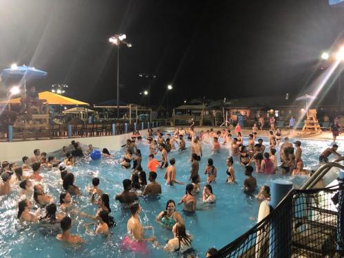 A crowded pool at night, filled with people enjoying the water under bright lights and colorful umbrellas.