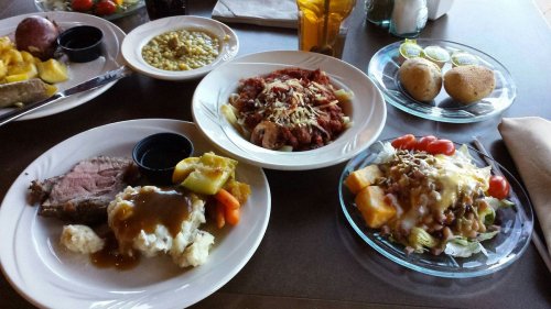 A table with three plates of food: roast beef with mashed potatoes, pasta with sauce, and a salad with toppings.