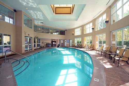 Indoor swimming pool with large windows, lounge chairs, and a bright, airy atmosphere.