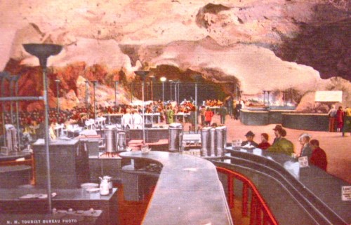 A large underground dining area with a curved counter, filled with people enjoying meals in a cave-like setting.