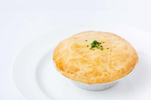 A golden-brown pie with a flaky crust, garnished with a sprinkle of green herbs, on a white plate.