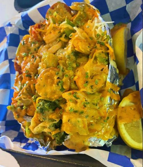 A foil-wrapped dish filled with colorful vegetables, shrimp, and a creamy sauce, served with lemon wedges on the side.