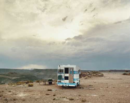 A vintage camper trailer sits alone on a barren landscape under a cloudy sky.