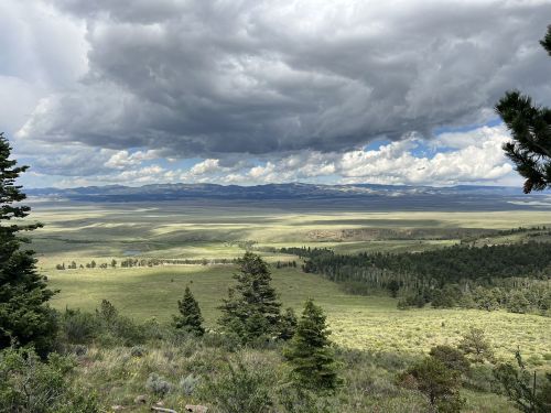 A panoramic view of rolling green hills under a cloudy sky, with distant mountains on the horizon.