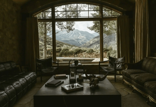 Cozy living room with a view of mountains through large windows, featuring a coffee table and comfortable seating.