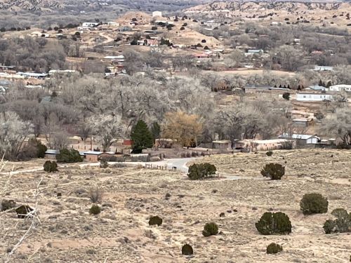 A panoramic view of a rural landscape with scattered homes, trees, and hills under a cloudy sky.