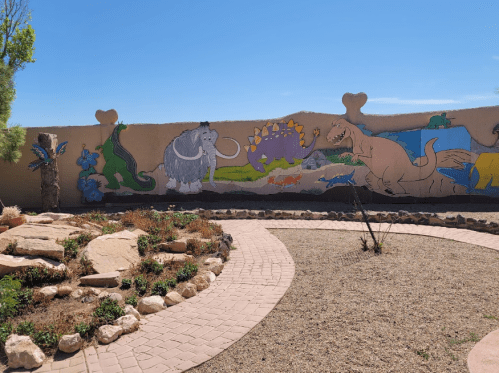 Colorful mural featuring various cartoon animals on a wall, surrounded by a landscaped garden with pathways.