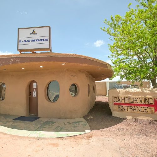 A round, adobe-style laundry building with a sign, next to a campground entrance under a clear blue sky.