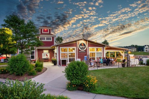 A cozy restaurant with outdoor seating, surrounded by greenery, under a colorful sky at sunset.