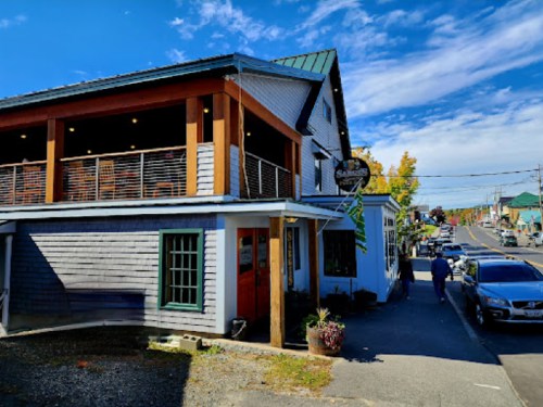 A charming two-story building with a wooden exterior, featuring a balcony and colorful signage, on a sunny street.