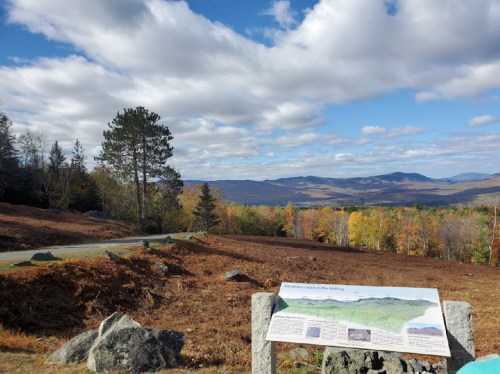 Scenic view of rolling hills and trees under a cloudy sky, with an informational sign in the foreground.