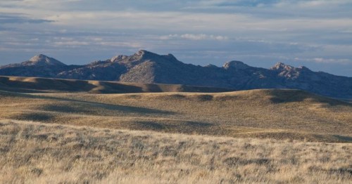 A vast landscape with rolling hills and distant mountains under a cloudy sky. Grassy plains in the foreground.