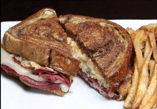 A grilled sandwich with layers of meat and cheese, served with a side of crispy fries.