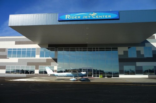 A small aircraft parked in front of the modern Rider Jet Center building with large windows and a blue sign.