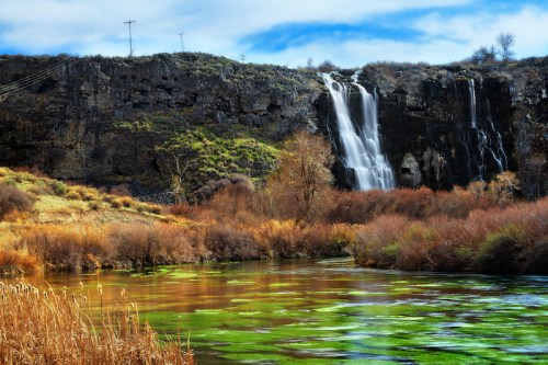 A serene landscape featuring a waterfall cascading down rocky cliffs, surrounded by lush greenery and a reflective river.