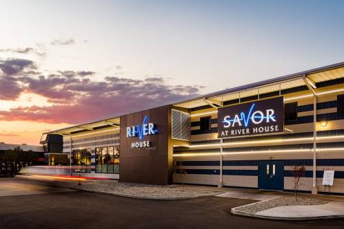 Exterior view of the River House building at sunset, featuring illuminated signs for "River" and "Savor at River House."