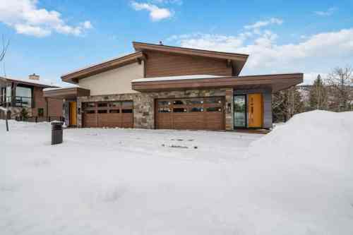 Modern house with stone accents and three garage doors, surrounded by snow under a clear blue sky.