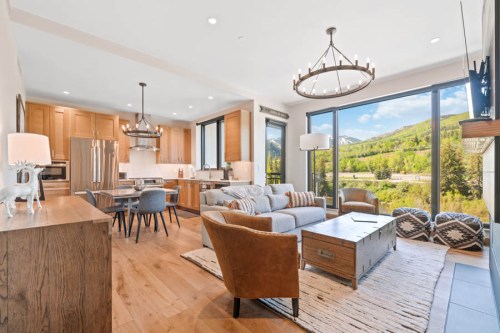 Modern living room with large windows, mountain views, wooden accents, and cozy furniture. Bright and inviting atmosphere.