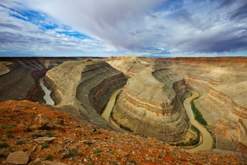 A winding river flows through a rugged canyon landscape under a cloudy sky.
