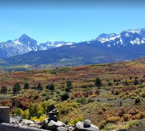 A scenic view of mountains with snow-capped peaks, surrounded by colorful autumn foliage and a clear blue sky.