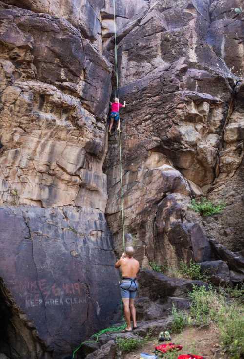 A climber ascends a rocky wall while a belayer secures the rope below in a natural outdoor setting.