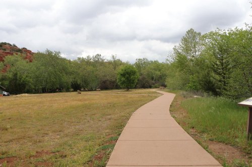 A winding path through a grassy area surrounded by trees under a cloudy sky.