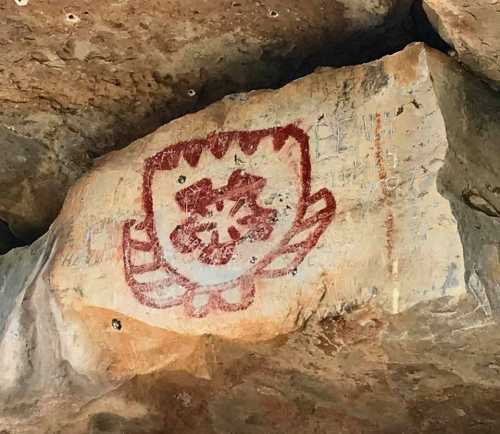 Ancient rock painting featuring a red flower-like design on a stone surface.