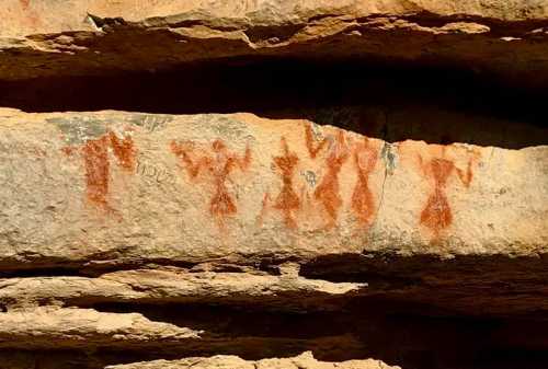 Ancient rock art featuring red figures on a stone surface, showcasing human-like shapes and symbols.