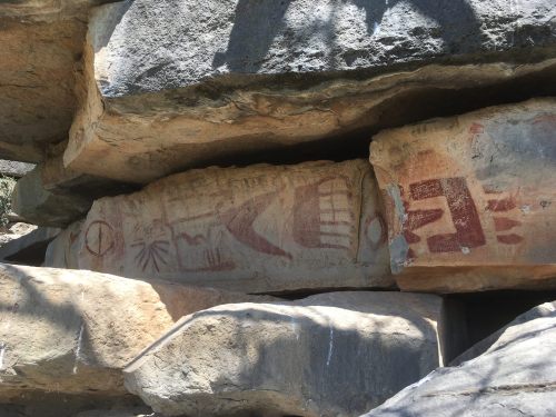 Ancient rock art featuring symbols and figures carved into stone, partially shaded by surrounding rocks.
