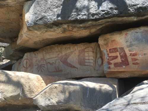 Ancient rock art featuring symbols and figures carved into stone, partially shaded by surrounding rocks.