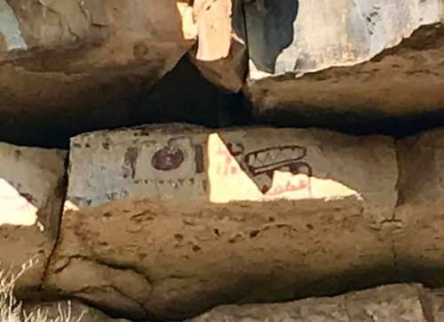 Ancient rock art featuring symbols and figures on a rocky surface, partially illuminated by sunlight.