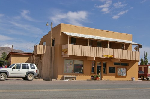 A two-story adobe building with a balcony, featuring a sign for a grocery store, set against a blue sky.